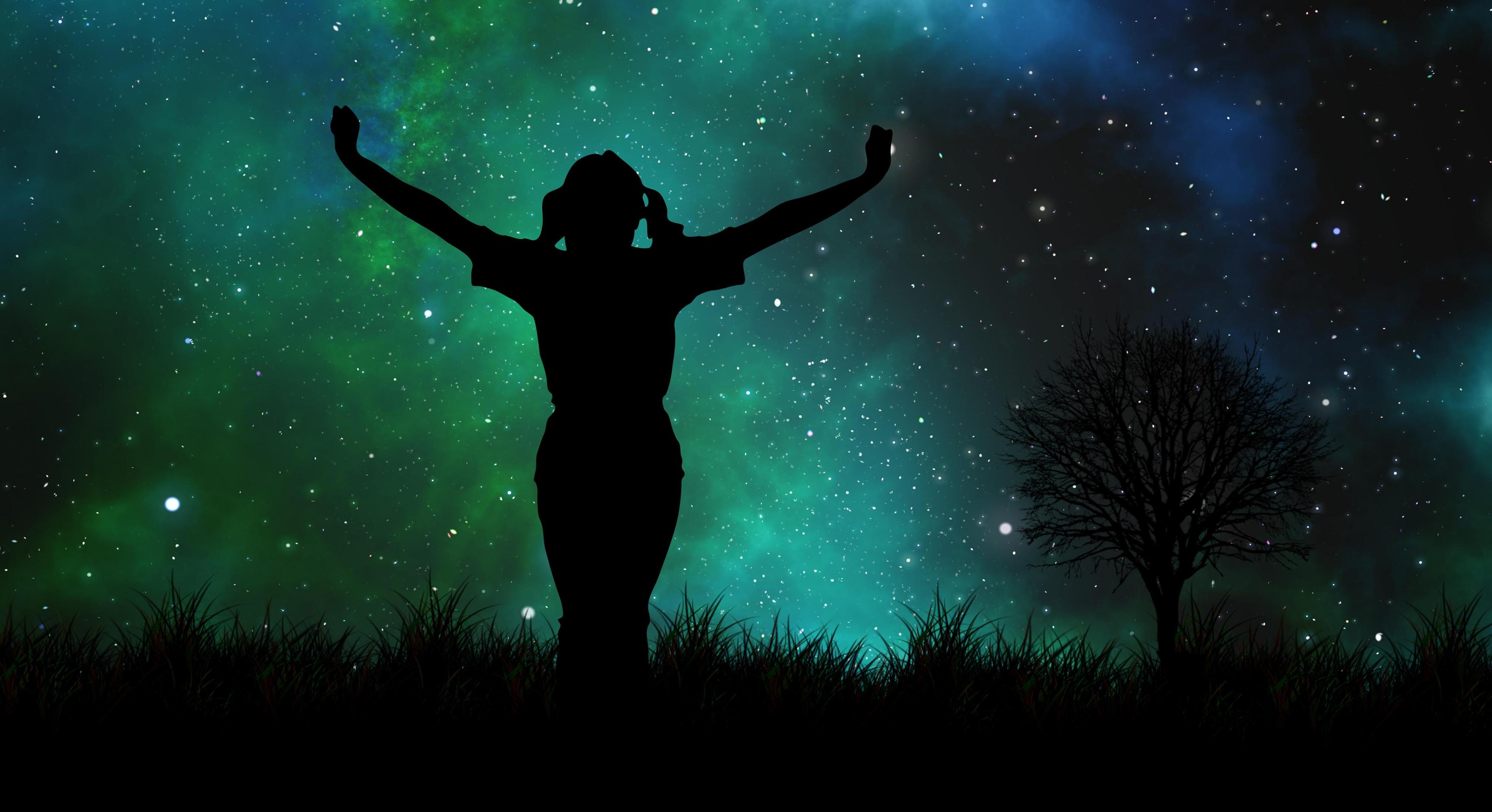 Silhouette of woman standing on hill in front of galaxy backdrop